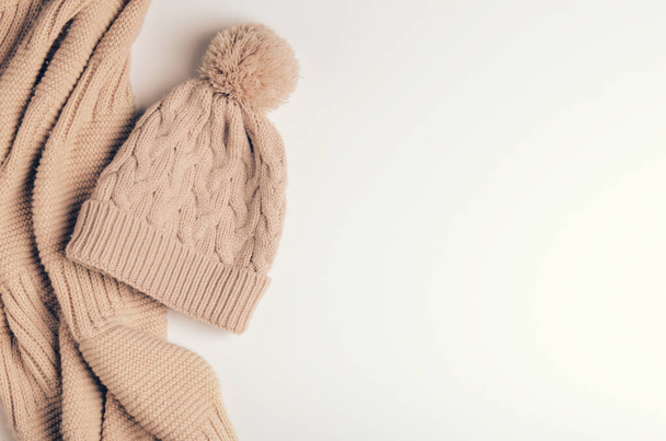 Sciarpa lavorata a maglia un tubo o un colletto da fili caldi e un berretto beige con un pompon. Accessori per autunno e inverno. Copia spazio, vista dall'alto, disposizione piatta
 - Foto, immagini