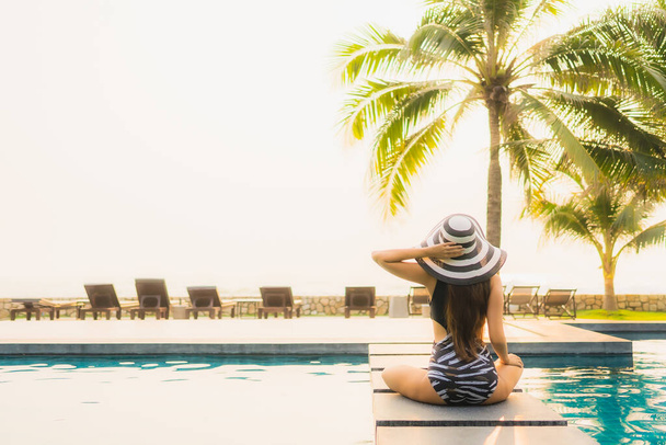 Πορτρέτο όμορφη νεαρή Ασιάτισσα γυναίκα χαλαρώστε γύρω από εξωτερική πισίνα στο θέρετρο του ξενοδοχείου με φοίνικα στο ηλιοβασίλεμα ή την ανατολή του ηλίου για διακοπές αναψυχής - Φωτογραφία, εικόνα