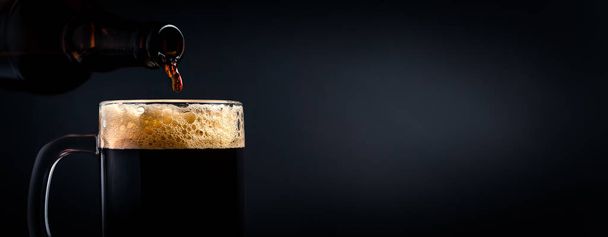 Une tasse de bière noire coulant d'une bouteille en gros plan, sur un fond sombre. Photo de stock
. - Photo, image