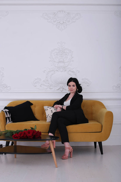  woman of thirty in a good mood in a trouser suit sits on a yellow sofa - Fotografie, Obrázek