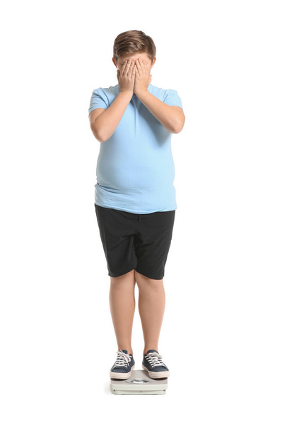 Overweight boy standing on scales against white background - Foto, afbeelding