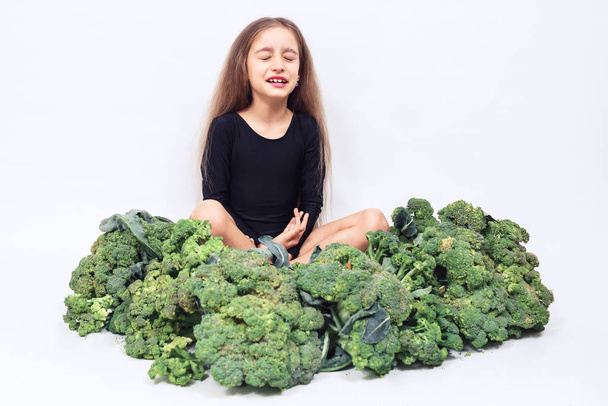 Το κοριτσάκι κάθεται σε ένα σωρό μπρόκολο και κλαίει. Στο παιδί δεν αρέσει να τρώει λαχανικά. - Φωτογραφία, εικόνα