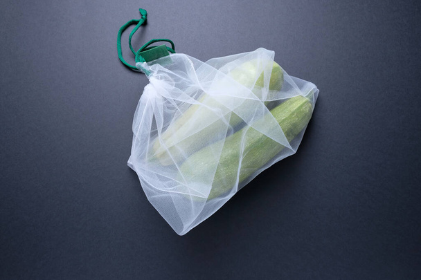 Composition with zucchini in a string bag on a black background. Eco concept, healthy food, vitamins. Zero waste concept. - Fotó, kép