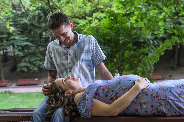 Young couple in love, husband and pregnant wife on a bench in the park, happy family - Photo, Image