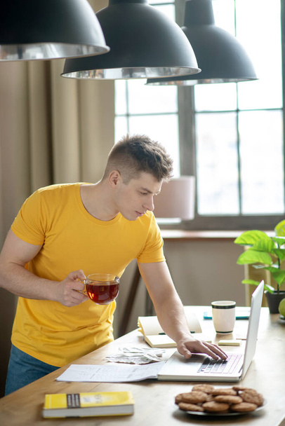 Young fair-haired man in yellow tshirt checking emails - Foto, imagen