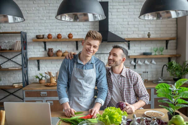Young gay couple making breakfast together and smiling - 写真・画像