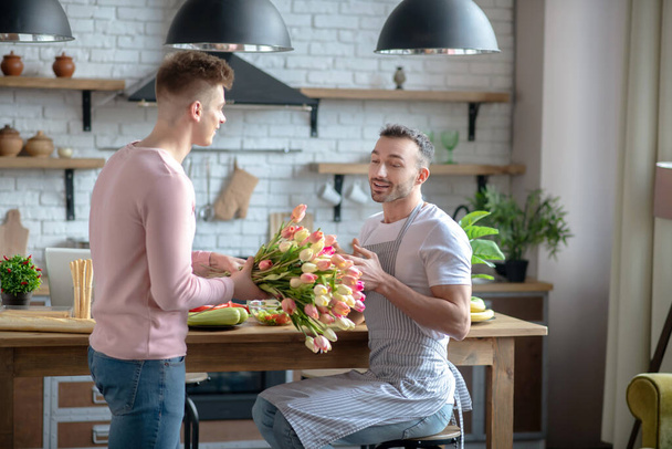 Standing man giving a bouquet of tulips to the seated. - Foto, afbeelding