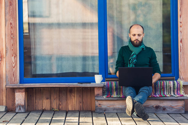 bearded freelancer works on laptop, sitting on steps of private house - Foto, Bild