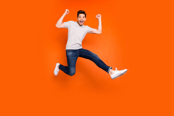 Full length photo of attractive crazy guy jump high supporting favorite football team match game goal wear striped t-shirt jeans shoes isolated bright orange color background - Fotoğraf, Görsel