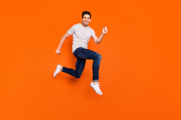 Full body profile photo of attractive crazy jump high rush shopping center addicted shopper discounts wear striped t-shirt jeans shoes isolated bright orange color background - Foto, Imagem