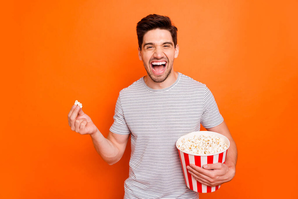 Photo of attractive crazy funky guy watch television humor show eat popcorn laughing out loud wear striped t-shirt isolated bright orange color background - Фото, зображення