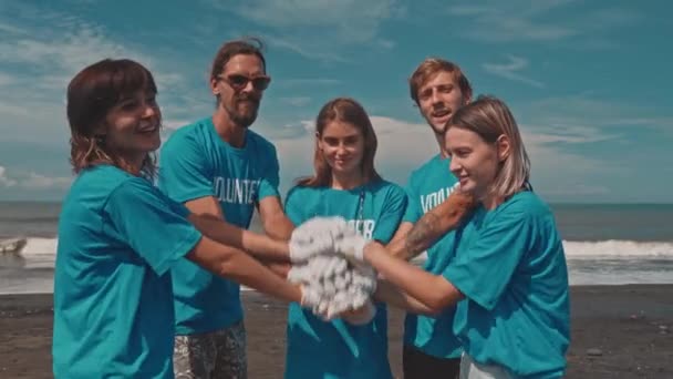 Group volunteers putting hands on top as symbol of unity for scavenging beach - Footage, Video