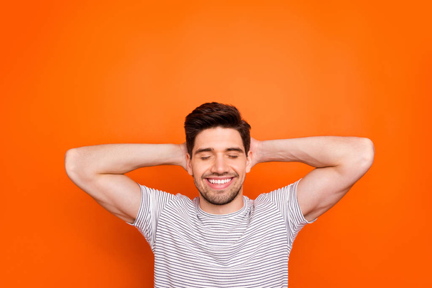Photo of attractive guy hold hands behind head relaxation moment eyes closed toothy beaming smile best weekend wear striped t-shirt isolated bright orange color background - Zdjęcie, obraz