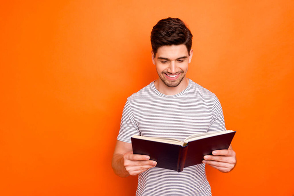 Photo of funny attractive guy hold favorite book hands enjoy reading exciting final intrigue wear striped t-shirt isolated bright orange color background - Φωτογραφία, εικόνα