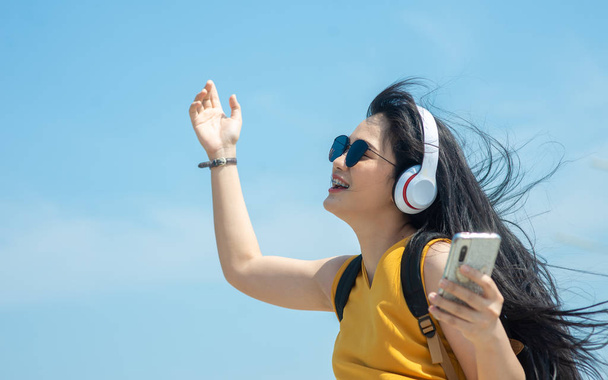 Happy Asian woman with backpack using headphone on the beach, lifestyle concept. - Foto, imagen