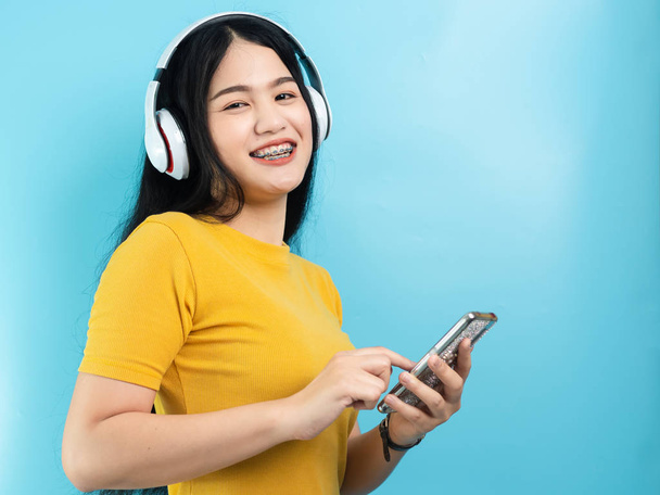Happy Asian woman using headphone and smartphone on blue background. - Foto, imagen