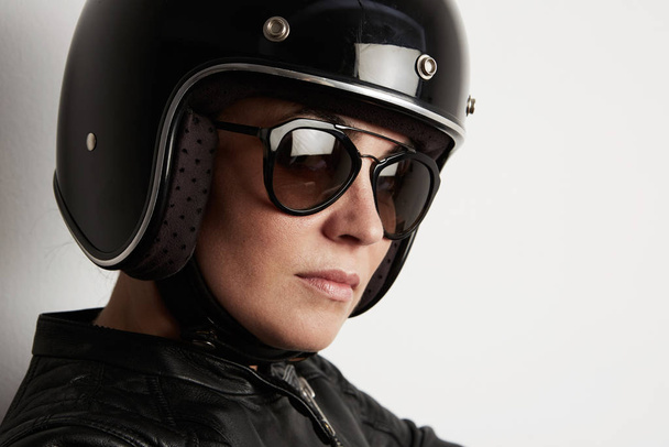 Close-up of attractive biker woman posing on the white wall and wearing black shiny helmet. - Foto, afbeelding