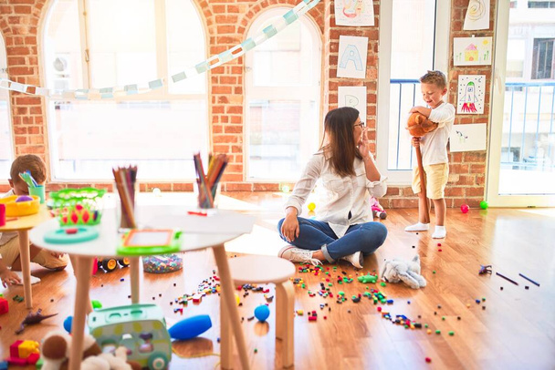 Hermosa maestra y niños pequeños jugando alrededor de un montón de juguetes en el jardín de infantes
 - Foto, Imagen
