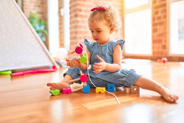 Hermoso bebé caucásico jugando con juguetes en la colorida sala de juegos. Feliz y juguetón con piezas de tren de madera en el jardín de infantes
. - Foto, Imagen