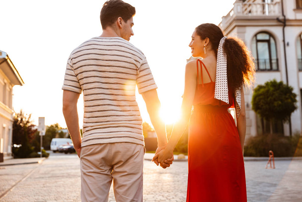 Kuva iloisesta valkoihoisesta pariskunnasta hymyilemässä ja pitämässä toisiaan kädestä kävellessään kaupungin kadulla
 - Valokuva, kuva
