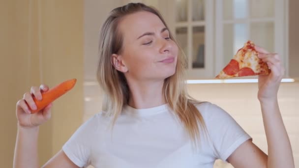Woman choosing pizza or carrot in kitchen - Footage, Video