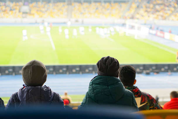 παιδιά παρακολουθούν ενώ απολαμβάνουν ένα παιχνίδι από τις θέσεις για τους θεατές στο γήπεδο - Φωτογραφία, εικόνα