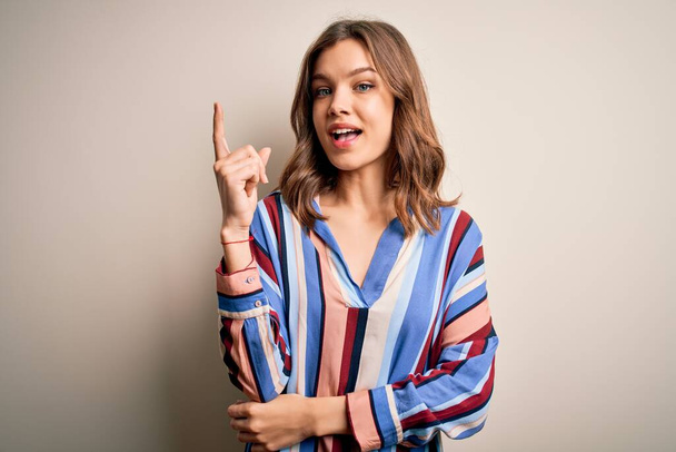 Young blonde girl wearing colorful striped shirt over isolated background pointing finger up with successful idea. Exited and happy. Number one. - Fotó, kép