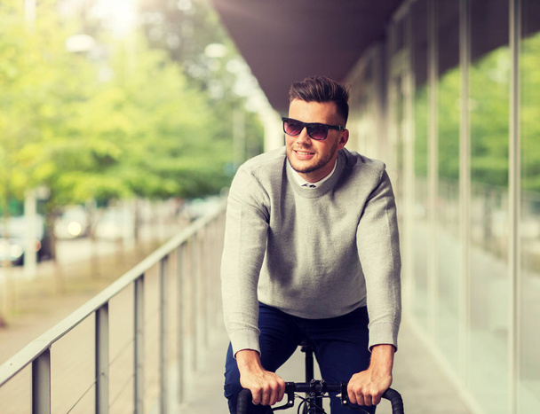 young man in shades riding bicycle on city street - Фото, изображение
