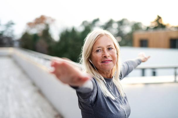 Uma mulher idosa com fones de ouvido ao ar livre fazendo exercício
. - Foto, Imagem