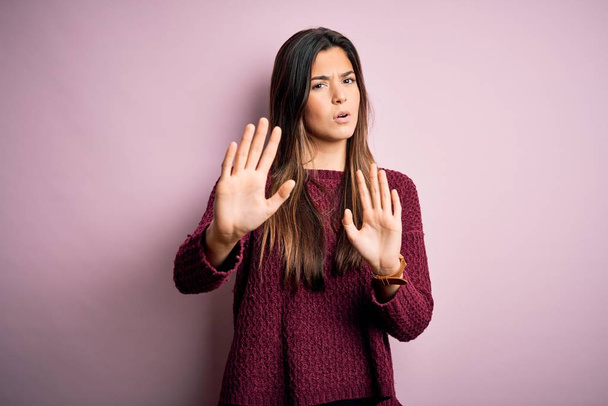 Young beautiful girl wearing casual sweater over isolated pink background Moving away hands palms showing refusal and denial with afraid and disgusting expression. Stop and forbidden. - Photo, Image