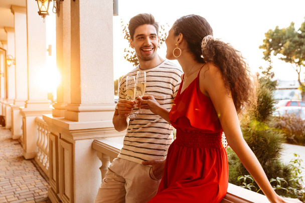 Image of beautiful smiling couple talking and drinking champagne near colonnades - Photo, Image