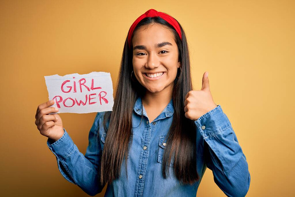 Junge schöne asiatische Frau trägt Diadema hält Banner mit Girl Power Botschaft glücklich mit großem Lächeln tun ok Zeichen, Daumen hoch mit den Fingern, hervorragende Zeichen - Foto, Bild