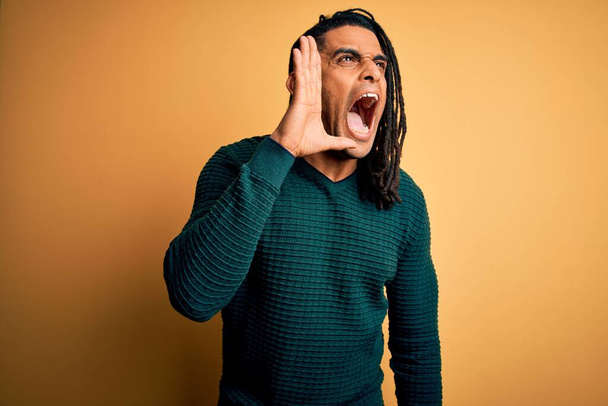 Young handsome african american afro man with dreadlocks wearing green casual sweater shouting and screaming loud to side with hand on mouth. Communication concept. - Photo, Image