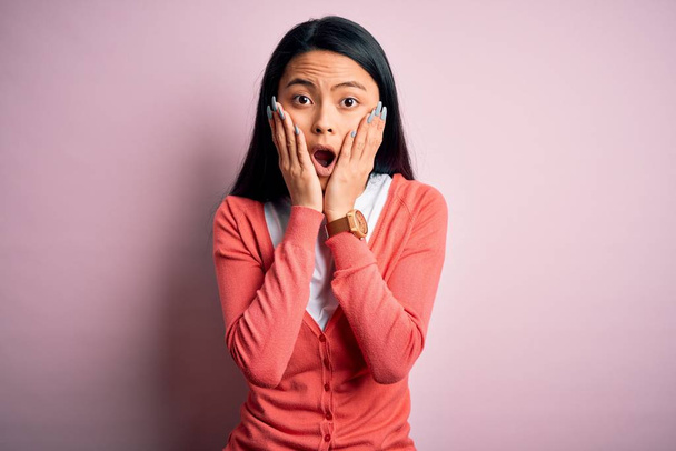 Молодая красивая китаянка в обычном свитере на изолированном розовом фоне испугана и шокирована, удивлена и поражена выражением лица
 - Фото, изображение