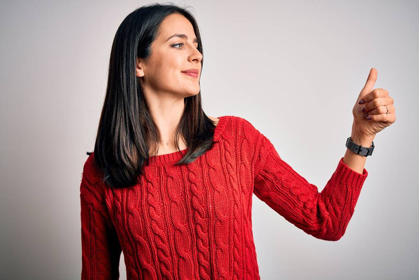 Young brunette woman with blue eyes wearing casual sweater over isolated white background Looking proud, smiling doing thumbs up gesture to the side - Photo, Image
