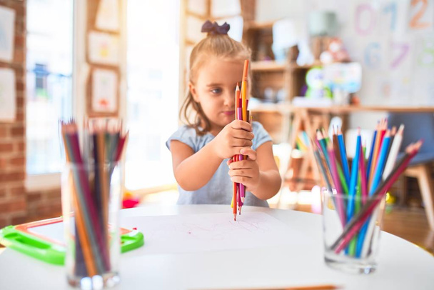 Jovem menina loira bonita que gosta de jogar escola com brinquedos no jardim de infância, sorrindo pintura feliz com cores lápis em casa
 - Foto, Imagem