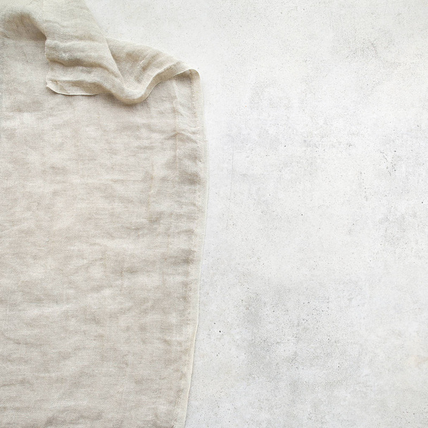 Pure washed linen cloth on light grunge stone background. Natural washed linen fabric on stone tile surface with copy space - Photo, Image