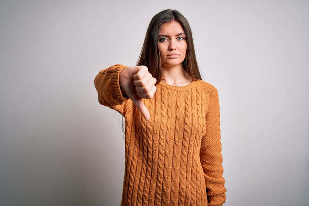 Young beautiful woman with blue eyes wearing casual sweater standing over white background looking unhappy and angry showing rejection and negative with thumbs down gesture. Bad expression. - 写真・画像