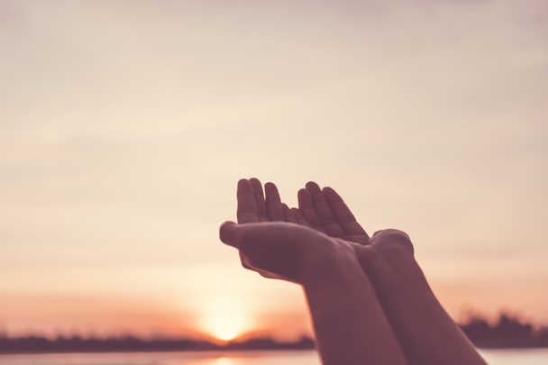 女性の手を一緒に自然のぼやけたビーチの前で祈るように配置夕日空の背景. - 写真・画像