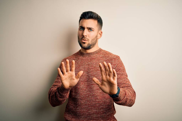 Young handsome man wearing casual sweater standing over isolated white background Moving away hands palms showing refusal and denial with afraid and disgusting expression. Stop and forbidden. - Фото, изображение
