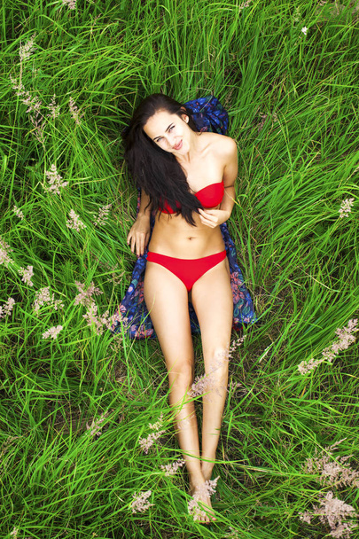 Young beautiful sexy girl in a red bathing suit lying on the grass top view - Foto, Imagen