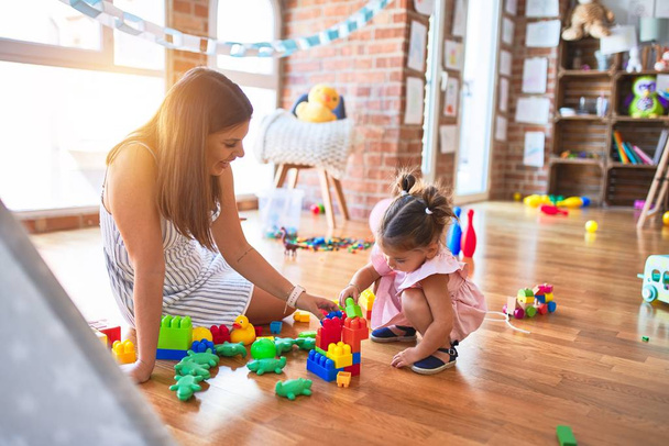 Молодой красивый учитель и ребенок сидит на полу, играя со строительными блоками игрушки в детском саду
 - Фото, изображение