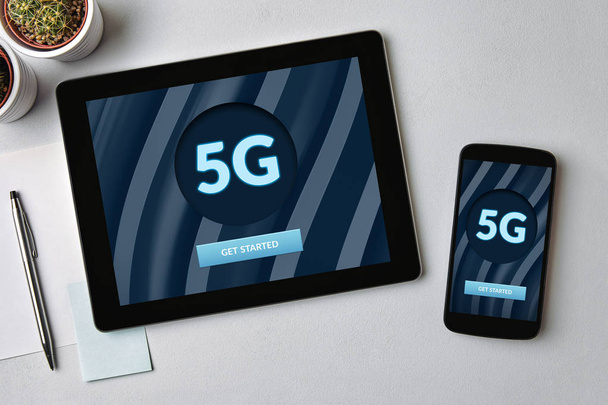 Concepto de red 5G en la tableta y la pantalla del teléfono móvil sobre la mesa gris. Vista superior
 - Foto, imagen