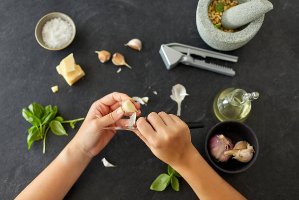 hands peeling garlic with knife for pesto sauce - Фото, зображення