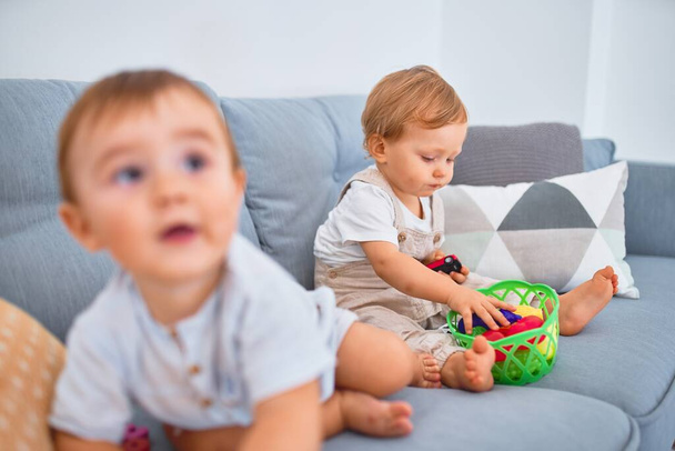 schöne Kleinkinder, die zu Hause auf dem Sofa sitzen und mit Spielzeug spielen - Foto, Bild