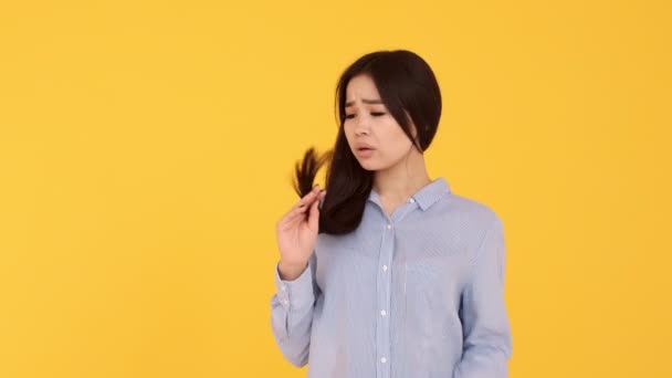 a young girl looks at the Asian women's hair split hair on a yellow background - Video