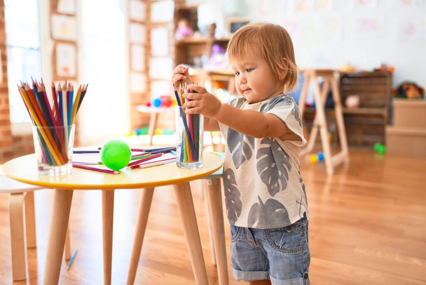 幼児は幼稚園でたくさんのおもちゃの周りに鉛筆を持っています - 写真・画像