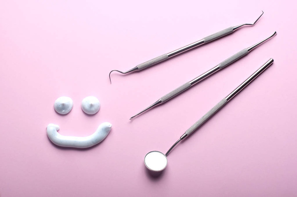 Ruostumattomasta teräksestä valmistetut hammasinstrumentit ja hammastahna hymyilevät kasvot vaaleanpunaisella taustalla
. - Valokuva, kuva