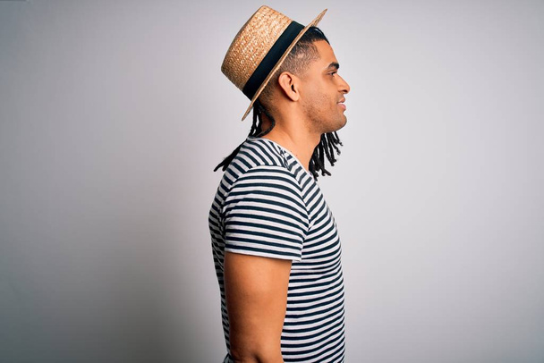 Young african american man with dreadlocks on vacation wearing striped t-shirt and hat looking to side, relax profile pose with natural face with confident smile. - Fotoğraf, Görsel