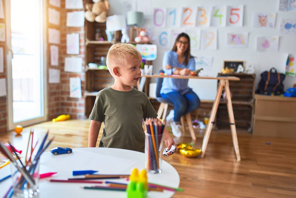 Mladé bělošské dítě hrající si s učitelkou na škole. Mladá žena sedící na stole ve třídě - Fotografie, Obrázek